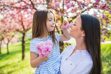 young mother holding small daughter outside in spring nature.