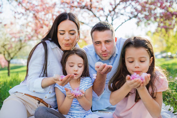 Wall Mural - Young parents with small daugthers sitting outside in spring nature.