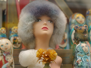 Photography of Mannequin of a woman in a fur hat. Large range of bright colorful Matreshka-dolls (traditional Russian wooden nesting toys) in the store. 