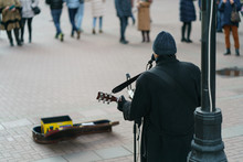 Photography Of A Street Musician Plays The Guitar On A City Street On A Spring Day.  There Is On The Pavement A Guitar Case For Money. Backs / Rear View. Festive Mood. Arbat Street.