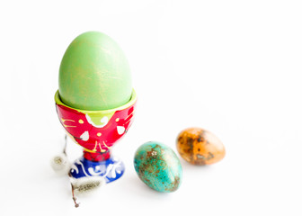 Wall Mural - Green egg in egg red stand and guail easter eggs on a white background, closeup, soft focus. Easter simbol. 	