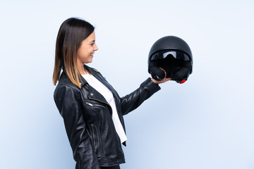 Wall Mural - Young brunette woman holding a motorcycle helmet over isolated blue background with happy expression