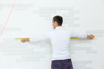 Master builder in uniform of measuring distances on a white wall with a tape measure