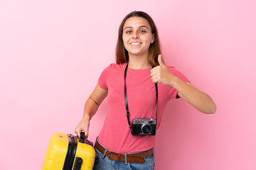 Teenager traveler girl holding a suitcase over isolated pink background with thumbs up because something good has happened