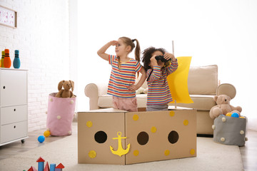 Cute little children playing with cardboard ship and binoculars at home