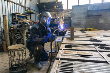 Wall Mural - A welder in a workshop manufactures and connects metal structures, a worker in a protective mask performs welding work.