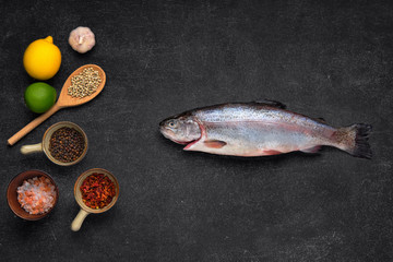 Sticker - Overhead view of fresh raw trout with spice on black stone background