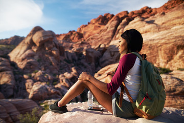 Wall Mural - female hiker sitting near cliff ledge at red rock canyon with smart phone and water bottle