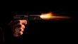 The hand presses the trigger of the gun and the flame from the shot escapes from its muzzle