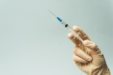 Doctor's hand in a white rubber glove holds a medical syringe on a blue background. The concept of medicine and medical care for the patient