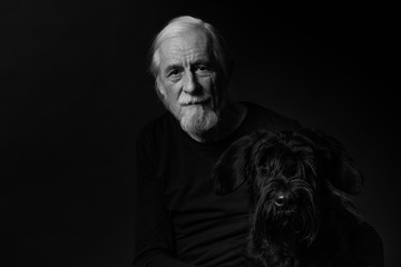 Wall Mural - Black and white low key studio portrait of beautiful gray hair old man and his Big Black Schnauzer Dog. 