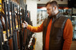 © Nomad_Soul - Man choosing rifle at showcase in gun shop