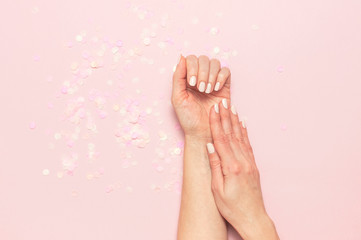 Wall Mural - Stylish fashionable female manicure in pastel colors. Hands of young girl on pink background with festive confetti. Minimalist manicure trend. Flat lay, top view, copy space. Natural nails, gel polish