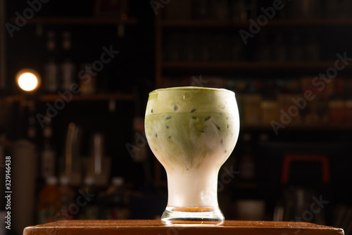 green tea separate layer with milk in curve glass with floating soft milk foam topping on wood table and coffee bar blur in background stock photo