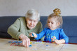 © Irina Schmidt - Beautiful toddler girl and grand grandmother playing together pictures lotto table cards game at home. Cute child and senior woman having fun together. Happy family indoors