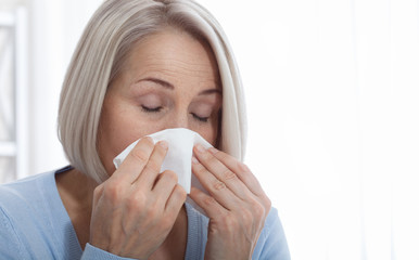 Healthcare, cold, allergy and people concept, sick woman blowing her runny nose in paper tissue on white background