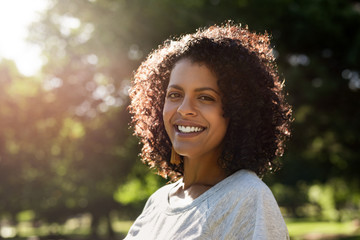 Wall Mural - Young woman standing in a park and smiling