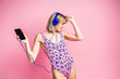 © Olga Rolencino - Sexy slim blonde woman posing in pink leopard swimsuit and earphones on a pink studio background and listening music from smartphone. Copyspace.