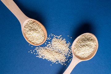 Two wooden spoons with white Flax seeds on blue background, flat lay.