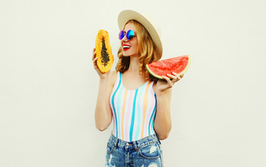 Summer portrait attractive smiling woman with slice of watermelon and papaya wearing straw hat, sunglasses, shorts over white background