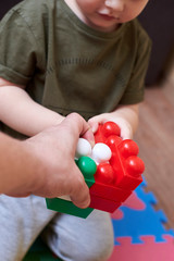 Wall Mural - Hands of dad and son playing with a colorful constructor set.