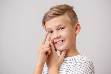 Poster - Little boy putting in contact lens on grey background