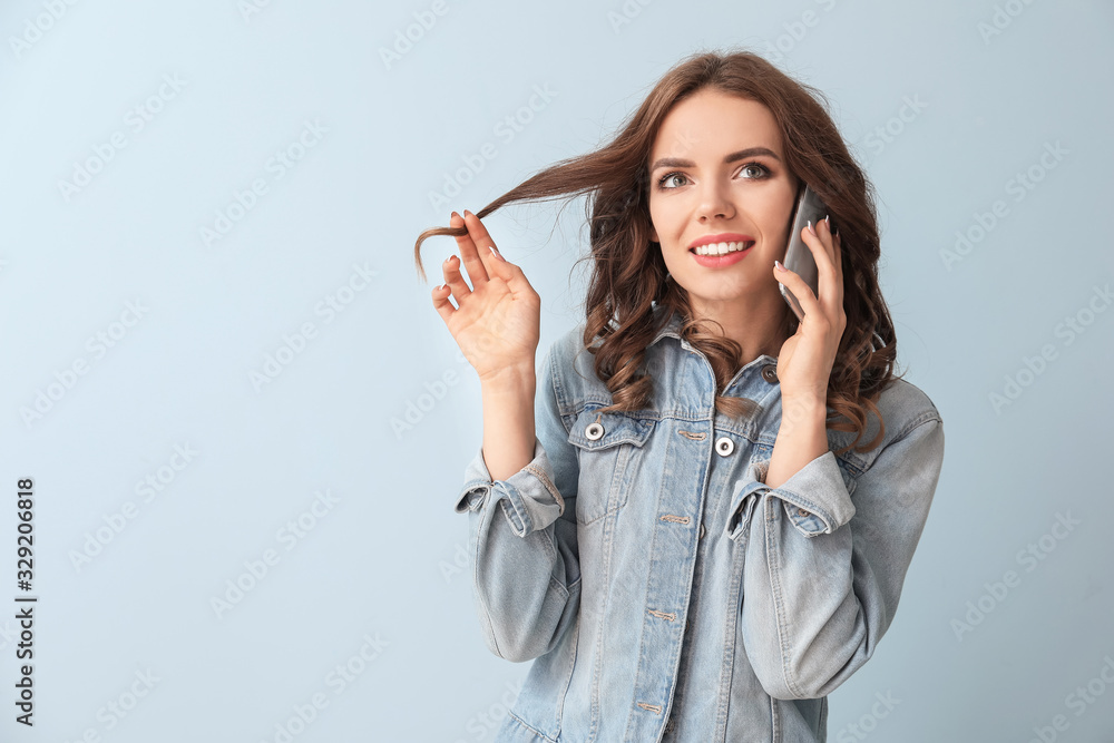 Young woman talking by mobile phone on color background