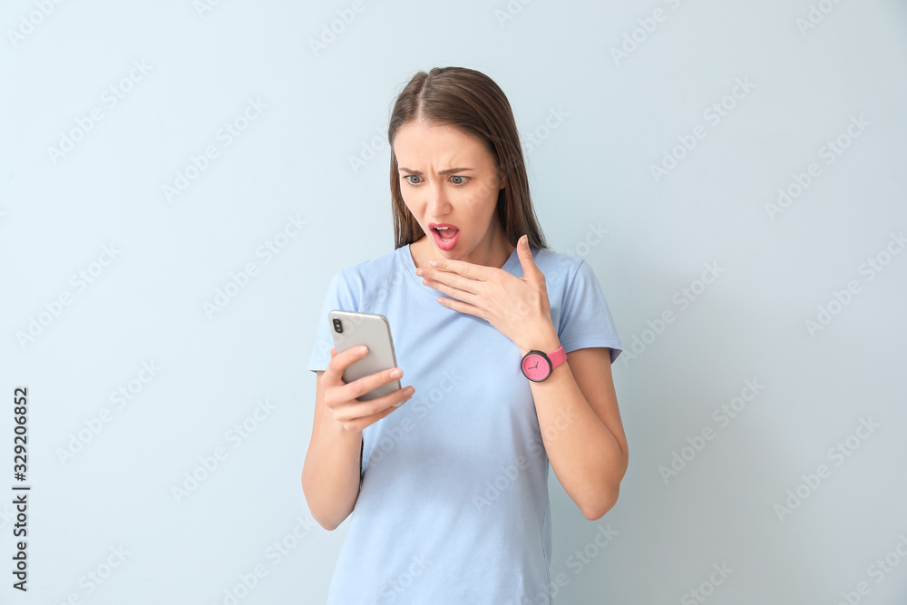 Shocked young woman with mobile phone on color background