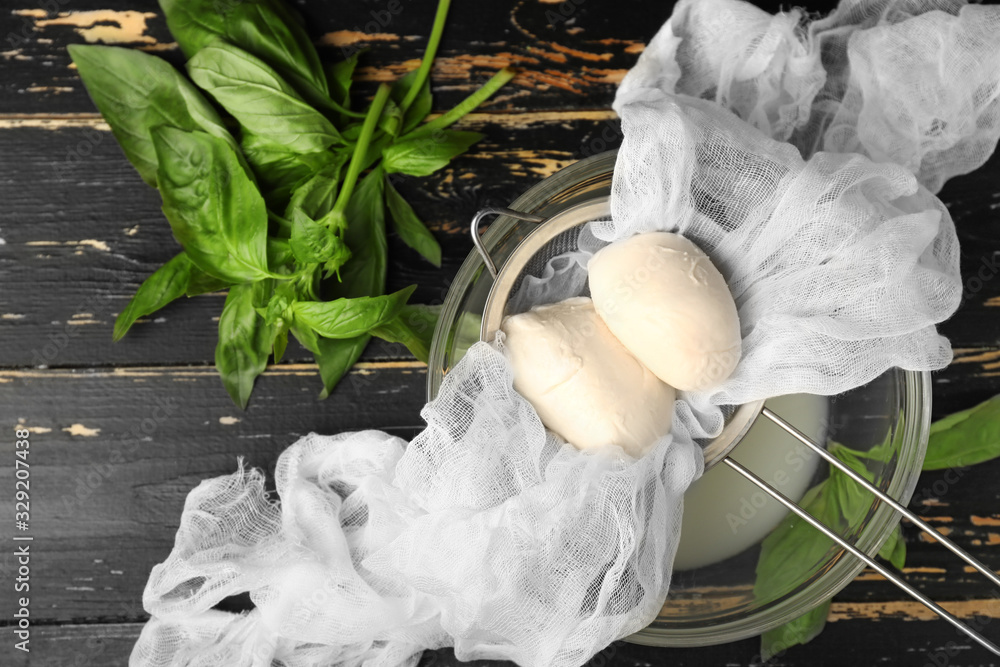 Sieve and bowl with mozzarella cheese on dark wooden background