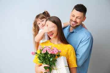 Husband and little daughter greeting woman to Mother's Day on grey background