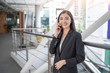© Have a nice day  - asian business woman holding a smartphone with calling or answering someone while smiling, on top of a platform standing next to the railing inside an open building with buildings in the background.