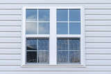 Double hung window with fixed top sash and bottom sash that slides up, sash divided by white grilles a surrounded by white elegant frame  horizontal white vinyl siding on a new construction residence