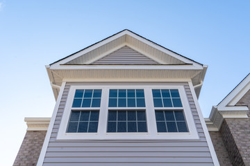 Double hung window with fixed top sash and bottom sash that slides up, sash divided by white grilles a surrounded by white elegant frame on a horizontal vinyl siding, under a gable and soffit