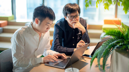 Business meeting and partnership concept. Asian man colleagues discussing about startup project using laptop computer and digital tablet in office. Coworkers team sharing ideas together at workplace.
