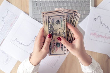 Time lapse. Woman freelancer holding banknotes fifty U.S. dollars in hand and counting profit, income. laptop with graphics and charts printed on the paper on office table. Flat lay