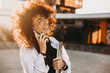 © Strelciuc - Cheerful caucasian lady with curly hair and eyeglasses is holding laptop while walking and talking on phone