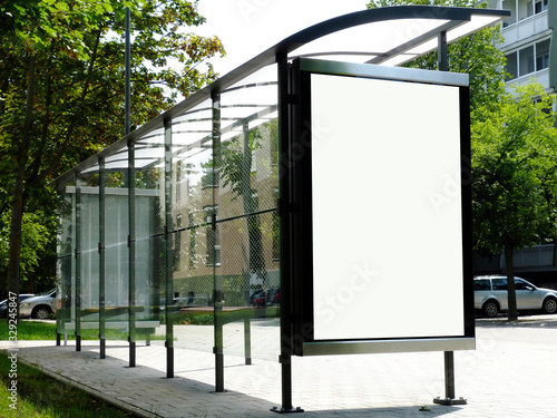 bus shelter at a bus stop. image collage of blank white glass & metal structure. urban setting with green background. safety glass design. white poster ad display. advertising concept. wooden benches.