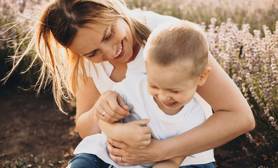 Caucasian blonde mother holding her son while having joy with him in a lavender field