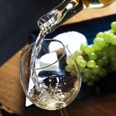 Wall Mural - Pouring white wine from bottle into the wineglass on the table