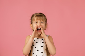 Wall Mural - child calling someone. cute little girl shouting and holding her hand near her mouth on studio pink background