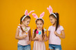 © producer - happy cute little child girls with pink bunny ears holding painted Easter eggs on studio yellow background. Easter day