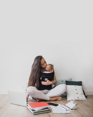 Mother working at home with baby in ergo backpack 