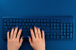 © fotofabrika - Woman hands typing on computer keyboard on classic blue background, top view
