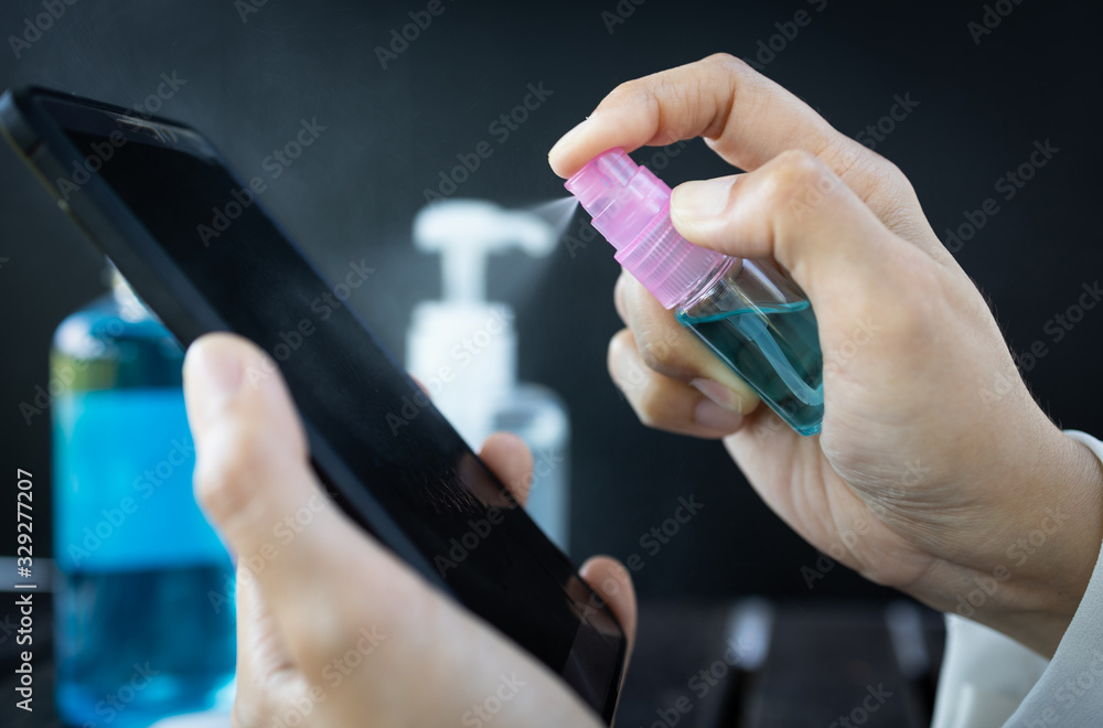 Hand of woman is spraying alcohol,disinfectant spray on mobile phone,prevent infection of Covid-19 virus,contamination of germs or bacteria,wipe or cleaning phone to eliminate,outbreak of Coronavirus - obrazy, fototapety, plakaty 