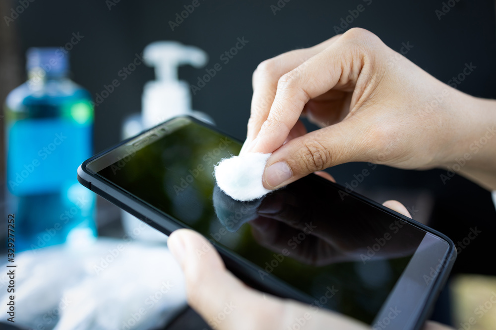 Hands of girl using cotton wool with alcohol to wipe on mobile phone to avoid contamination of Coronavirus,prevent contagious disease of Covid-19 virus,cleaning phone to eliminate of germs,bacteria - obrazy, fototapety, plakaty 