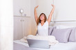 © Graphicroyalty - Woman stretching in bed after wake up in morning ready to work from home. Portrait of a young smiling woman sitting with laptop on bed. Freelance working from home concept