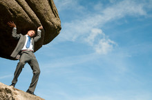 Strong Businessman Struggling To Lift Massive Boulder Into Blue Sky Copy Space
