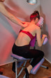 © Antonio - Back pain. Infrared heat light lamp therapy to a girl in a massage chair with red bra and sport trousers in a phisiotherapy clinic