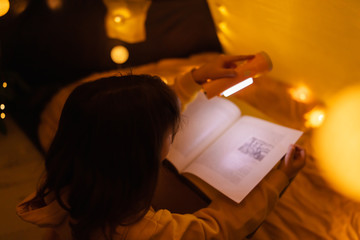 Wall Mural - young female child reading encyclopedia in a home made livingroom tent with light balls.