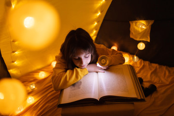 Wall Mural - young female child reading encyclopedia in a home made livingroom tent with light balls.